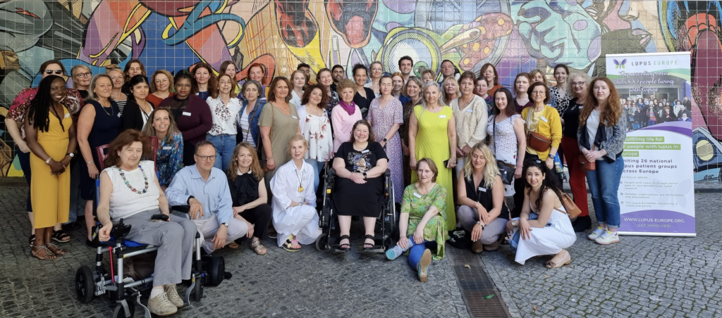 Group picture of Lupus Europe Convention 2023 Participants against a colourful wall background. On the right of the picture is the Lupus Europe banner. 