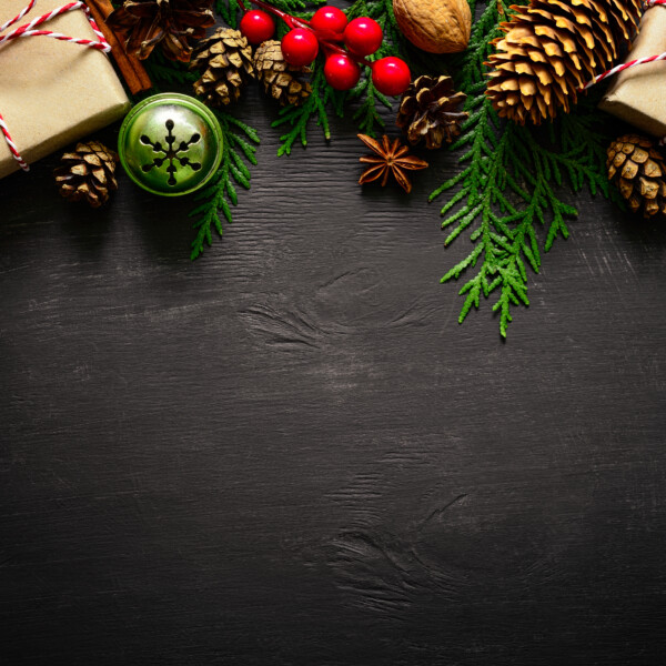 Festive Christmas background with evergreen branches, pine cones, red berries, walnuts, and a gift wrapped in kraft paper.